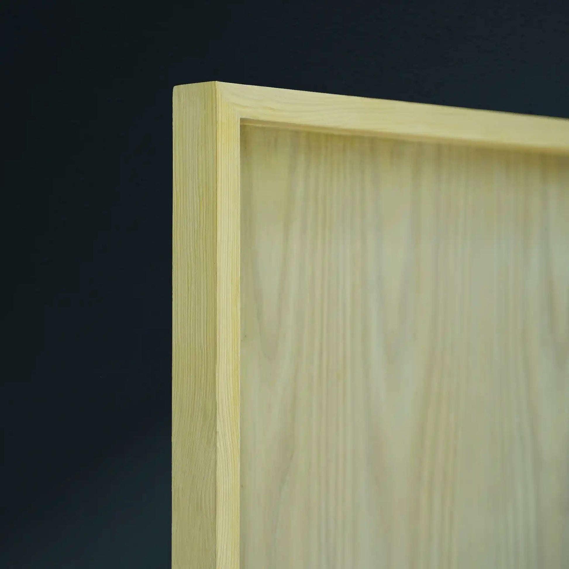 Close-up of a light natural wood framed board corner against a dark charcoal background.