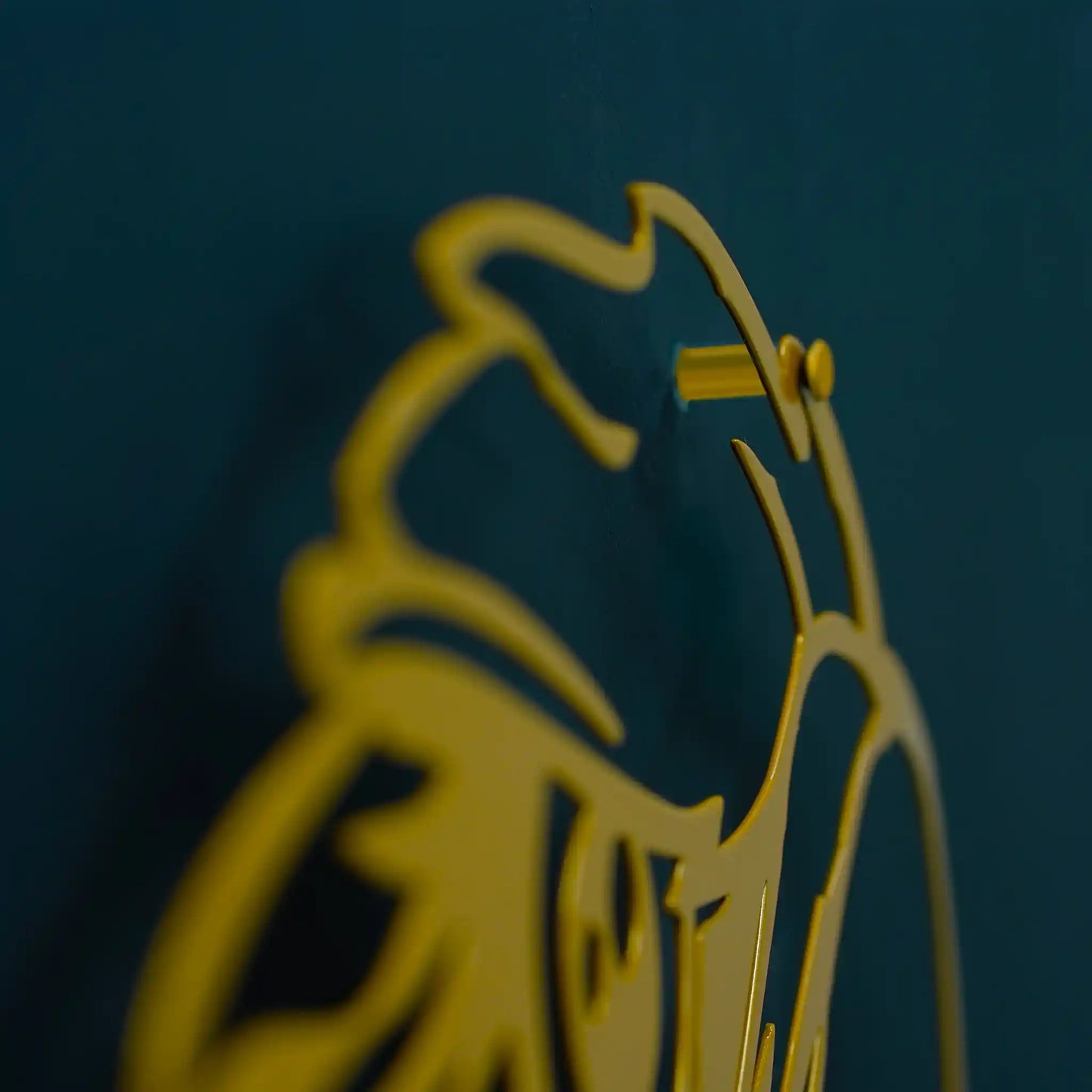 A close-up of a gold metal wall art of eagle head against a dark teal-blue background.