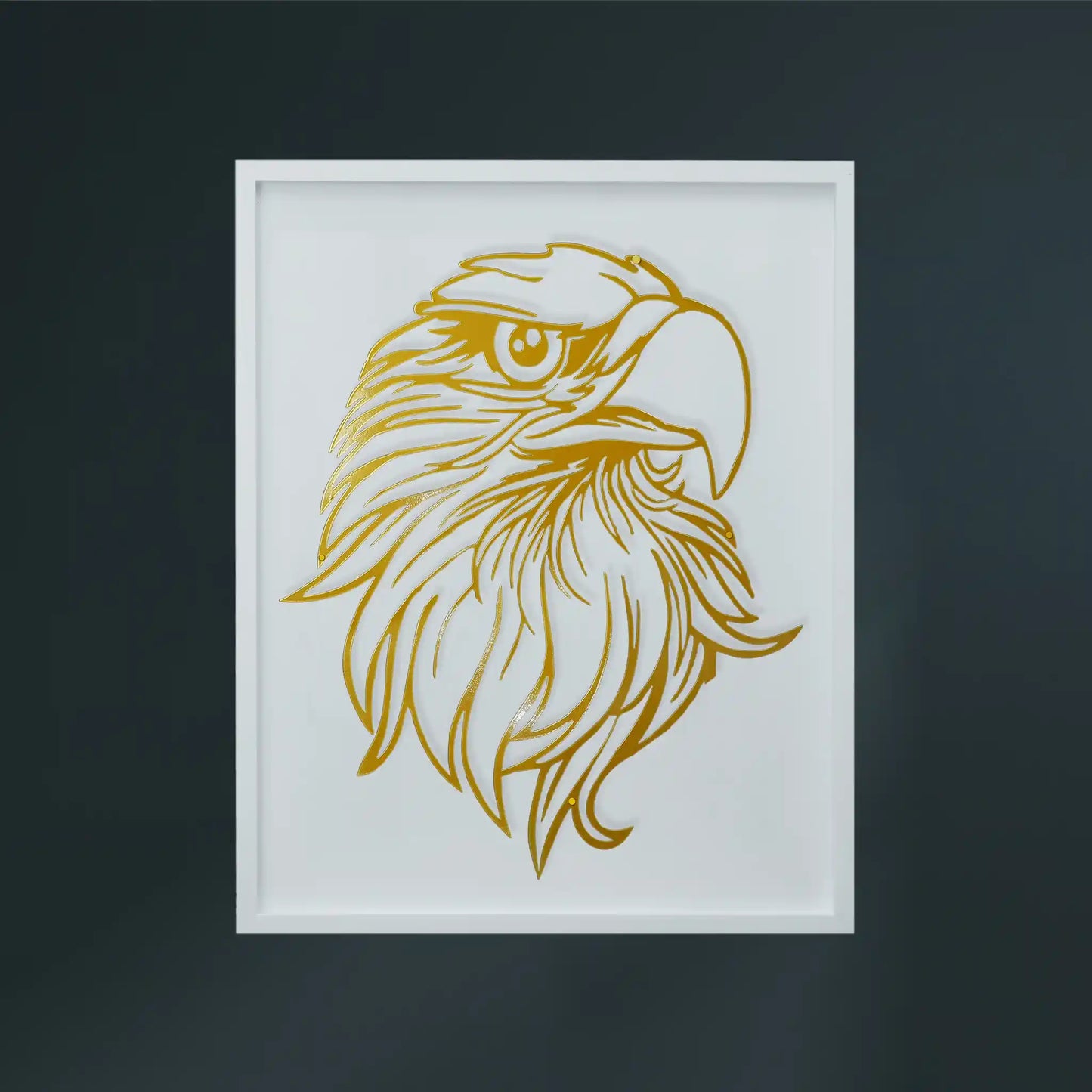 A framed metal wall art featuring a stylized golden eagle head illustration on a white wooden frame, set against a dark gray wall.