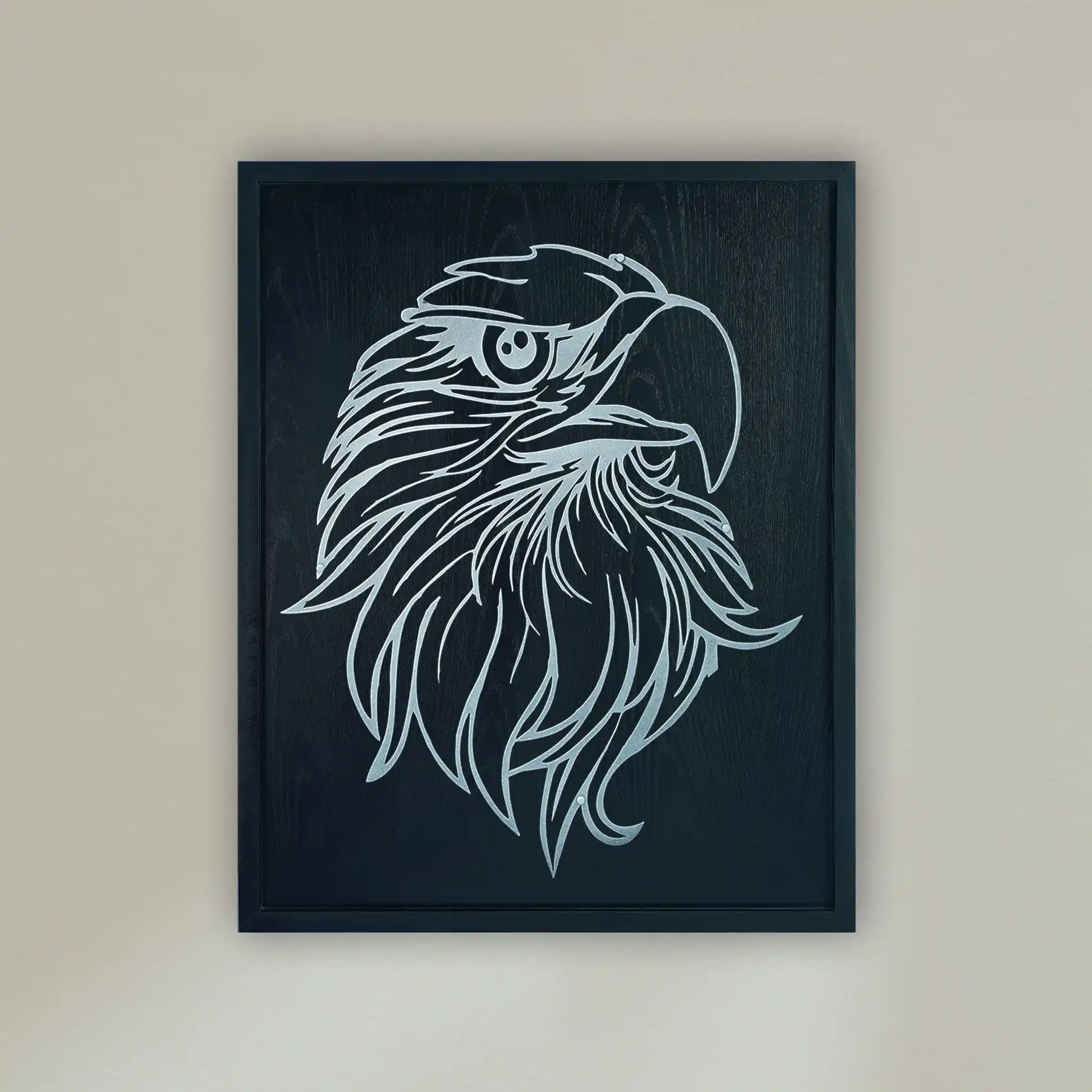 Framed wall art featuring a stylized metallic silver eagle head illustration on a black wood frame, hung on a light beige wall.