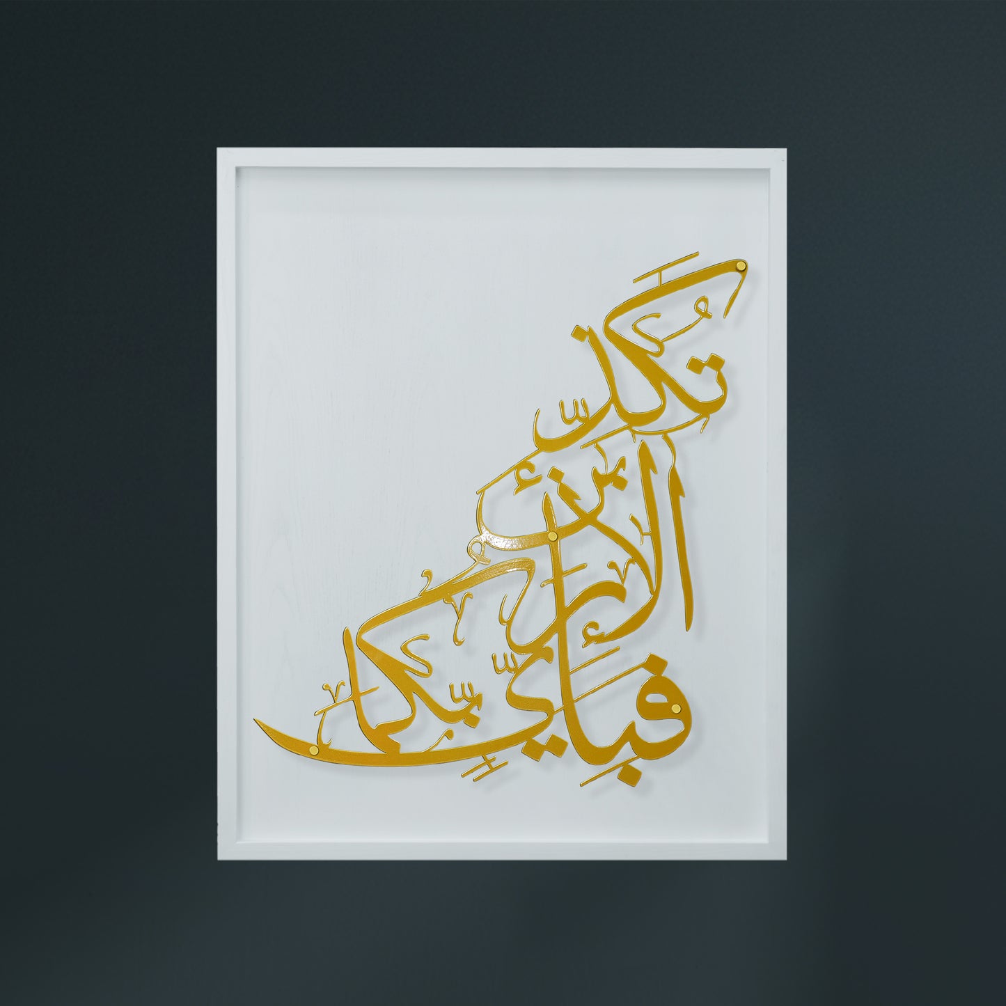 Gold Arabic calligraphy metal wall art mounted on a white wooden frame, shown against a dark charcoal background.