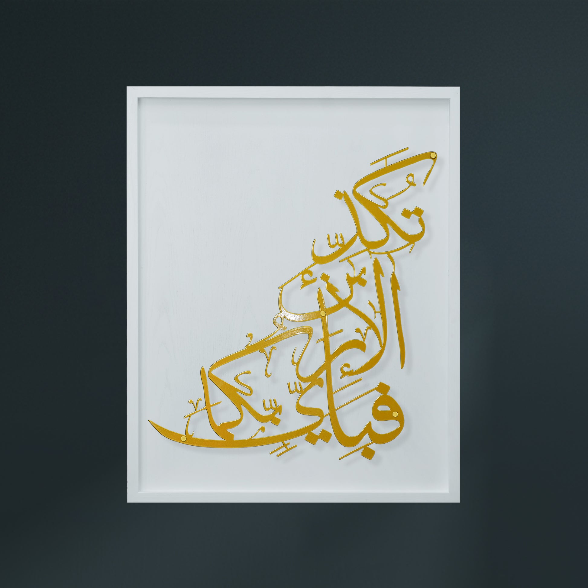 Gold Arabic calligraphy metal wall art mounted on a white wooden frame, shown against a dark charcoal background.