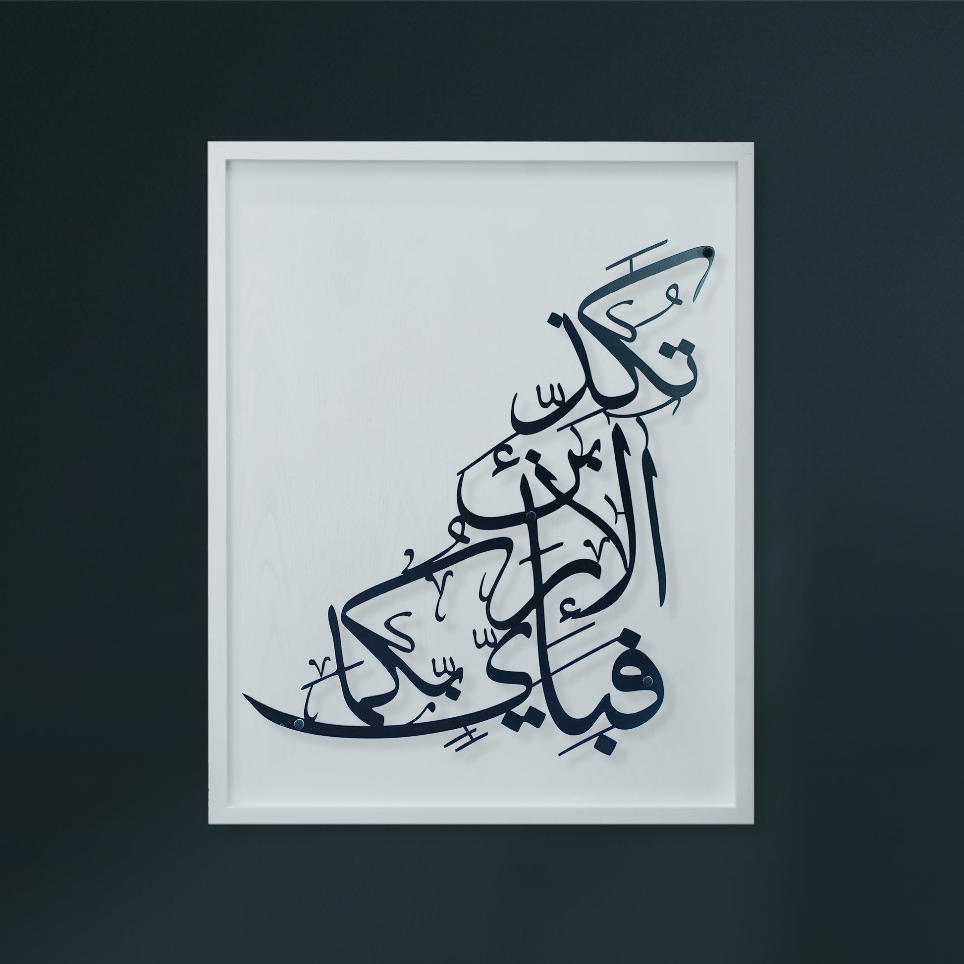 A framed Arabic calligraphy metal wall art  featuring black script on a white wooden, displayed against a dark charcoal wall.