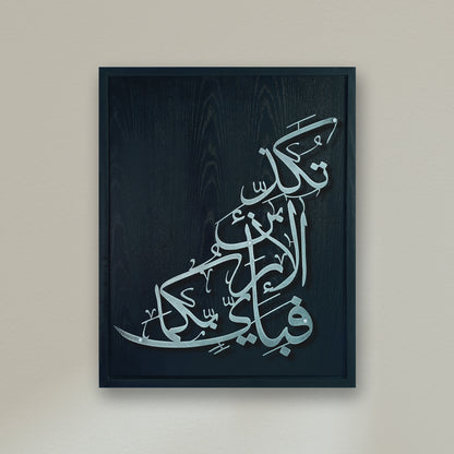 Framed Islamic wall art featuring elegant Arabic calligraphy in metallic silver on a black wooden frame, mounted on a neutral beige wall.