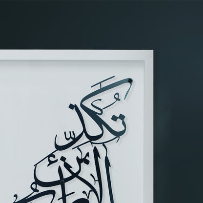 Close-up of a framed Arabic calligraphy metal wall art piece in black on a white wooden, mounted against a dark charcoal wall.