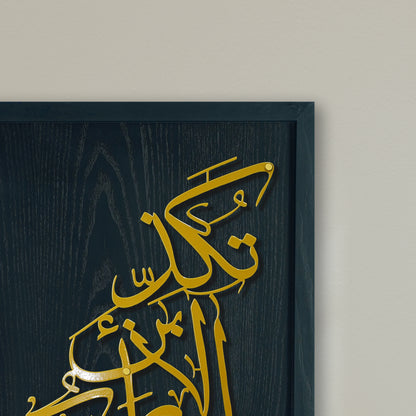 Gold Arabic calligraphy metal wall art mounted on a black wood panel, shown in a close-up against a light beige wall.