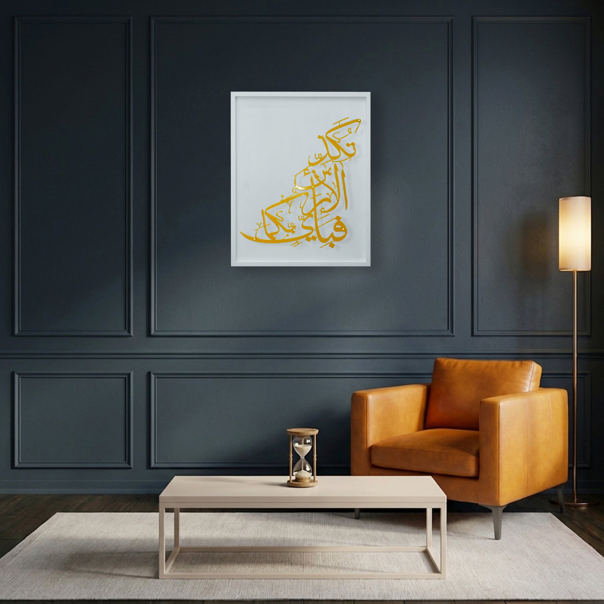 A framed Islamic calligraphy metal wall art in gold on a white wooden frame, displayed on a dark gray paneled wall above a modern orange armchair, a light wood coffee table, and a floor lamp.