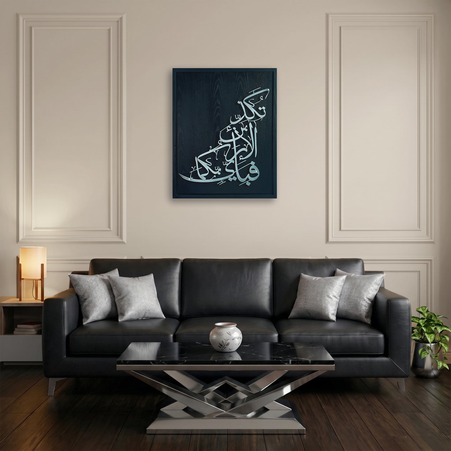 A framed vertical canvas print featuring silver Arabic calligraphy on a black wooden frame, displayed on a beige wall above a black leather sofa in a modern living room setting.