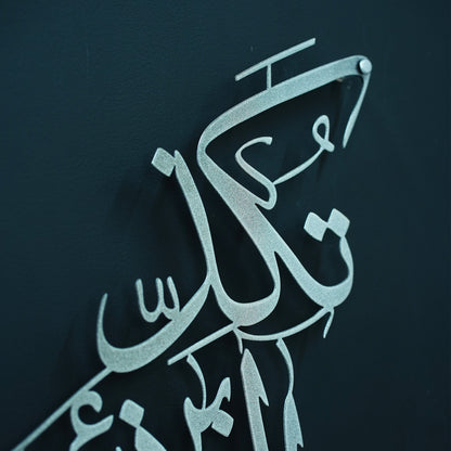 Silver Arabic calligraphy wall art mounted on a dark navy textured wall.