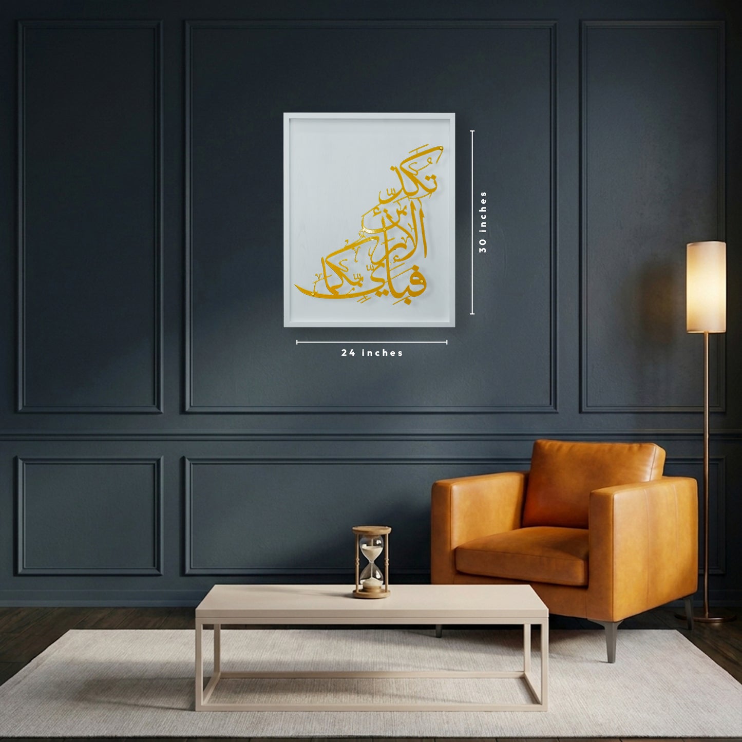 A framed piece of Arabic calligraphy metal wall art in gold and white wooden hangs on a dark navy paneled wall above a light wood coffee table and an orange leather armchair, with dimension labels showing 24 inches wide by 30 inches high.