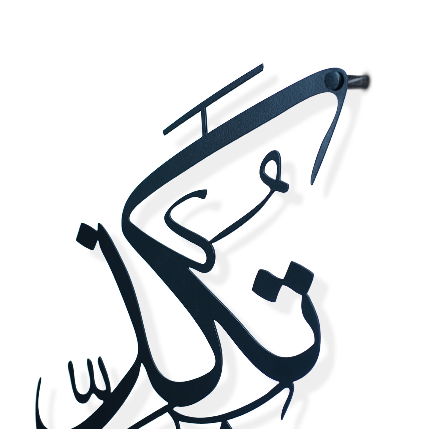 Black Arabic calligraphy metal wall art mounted on a plain white wall, shown at an angle with a soft drop shadow.