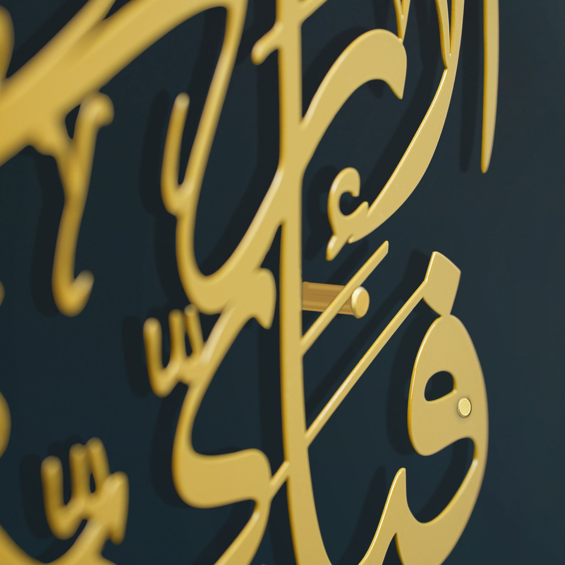 Close-up of a gold Arabic calligraphy wall art piece against a dark navy blue background.