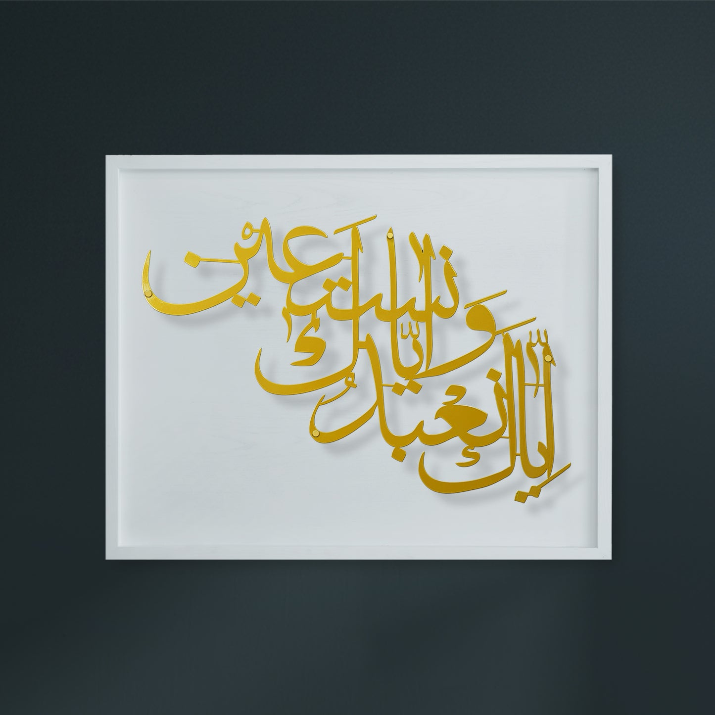 A white framed with metal wall art piece featuring elegant gold Arabic calligraphy on a white wooden, displayed against a dark charcoal wall