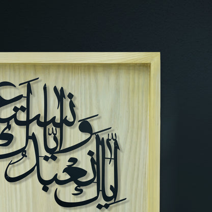 Black Arabic calligraphy metal wall art mounted on a light natural Diar color wooden frame, shown against a dark charcoal wall.