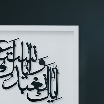Black Arabic calligraphy metal wall art mounted on a white wooden frame, shown against a dark charcoal wall.
