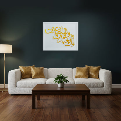 A framed metal wall art with gold Arabic calligraphy on a white wooden frame, displayed above a modern white boucle sofa in a dark living room with a wooden coffee table and wood floor.