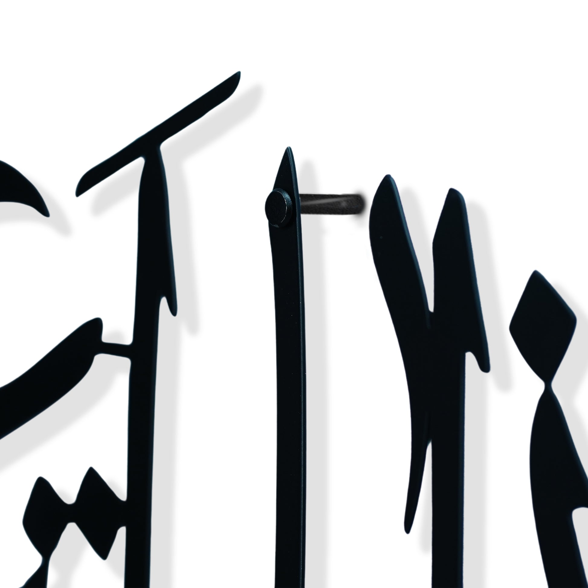 Close-up of a black metal wall art piece featuring stylized calligraphic letterforms on a white background.