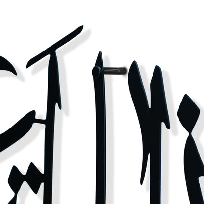 Close-up of a black metal wall art piece featuring stylized calligraphic letterforms on a white background.
