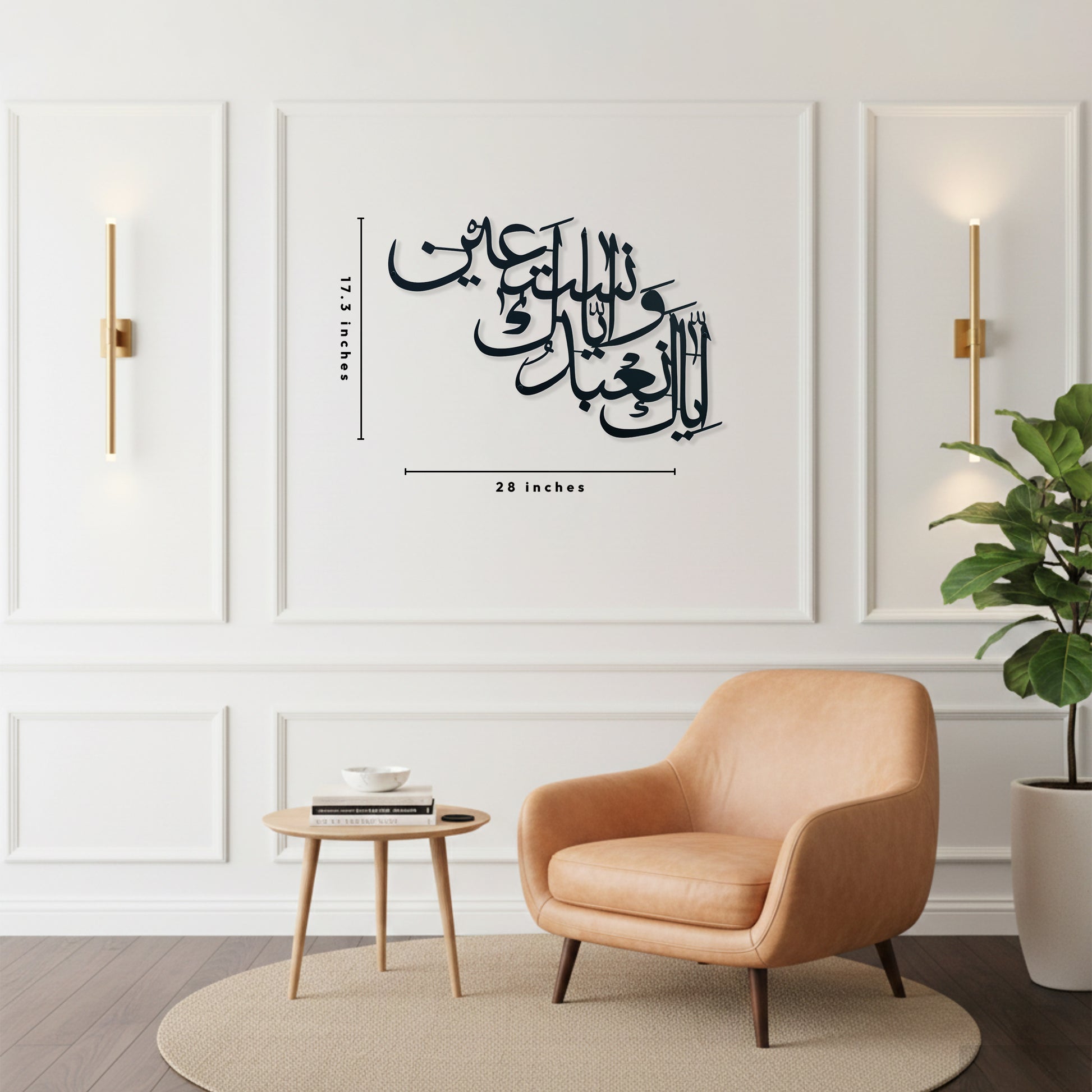 Black Arabic calligraphy metal wall art displayed on a white paneled wall in a modern living room setting, with a peach armchair, side table, and potted plant visible below. The calligraphy is shown with dimension markings indicating 28 inches wide by 17.3 inches tall.