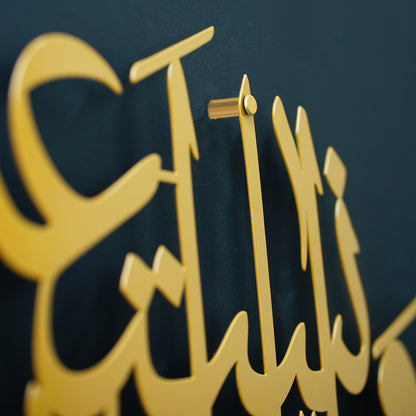 Gold metal Islamic metal wall art featuring elegant Arabic calligraphy, shown in a close-up shot against a dark textured background.