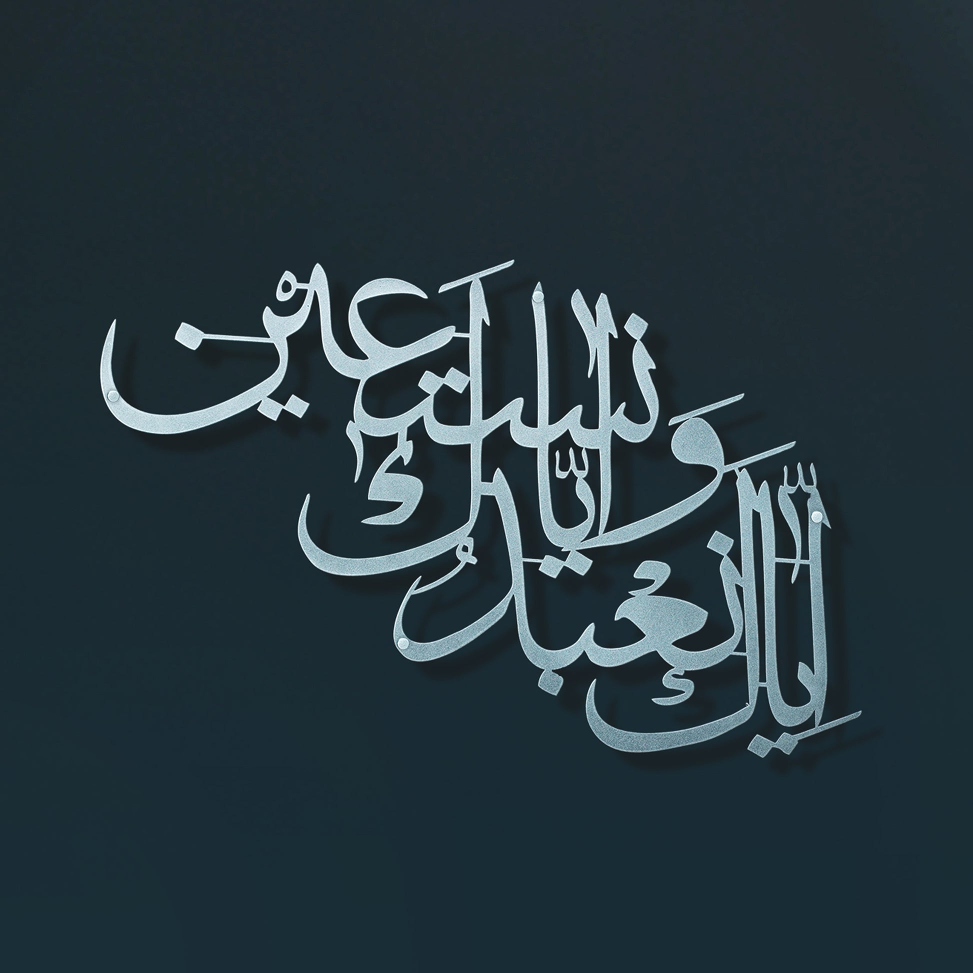 Arabic calligraphy metal wall art in a metallic silver tone on a dark teal background.