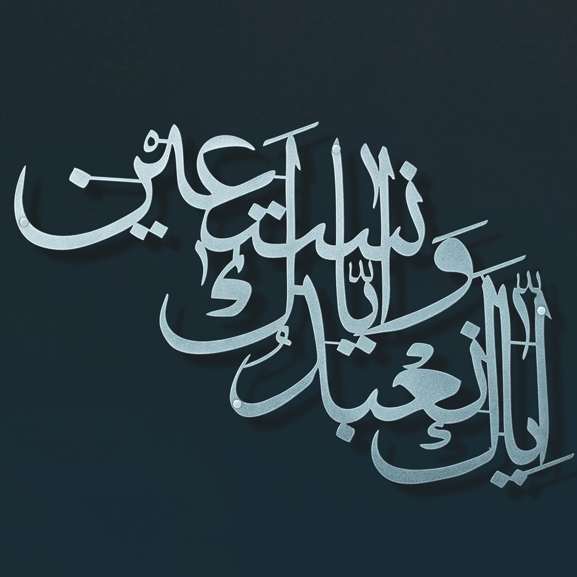 Silver Arabic calligraphy metal wall art shown against a dark navy blue background.