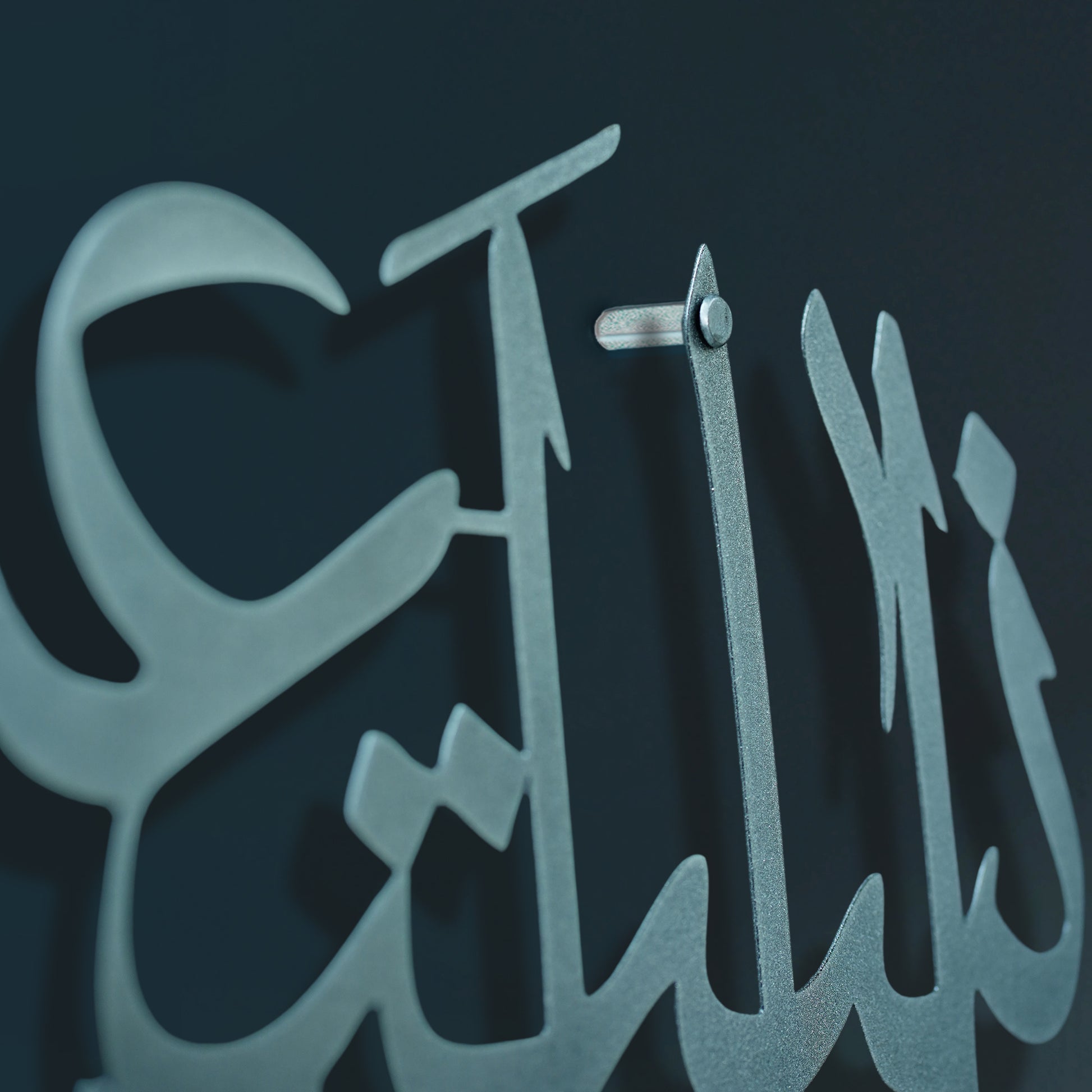 A close-up of a islamic calligraphy metal wall in a stylized font, mounted against a dark background.