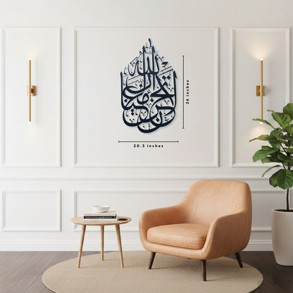 A styled interior room with a peach armchair, small round side table, potted plant, and wall sconces. The focal product appears to be the wall art: a dark black Arabic calligraphy La Tahzan İnnallahe Maana, Metal Wall Art piece mounted in the center of a white paneled wall. The image includes dimension lines indicating the frame is length 26 inches and width 20.3 inches.