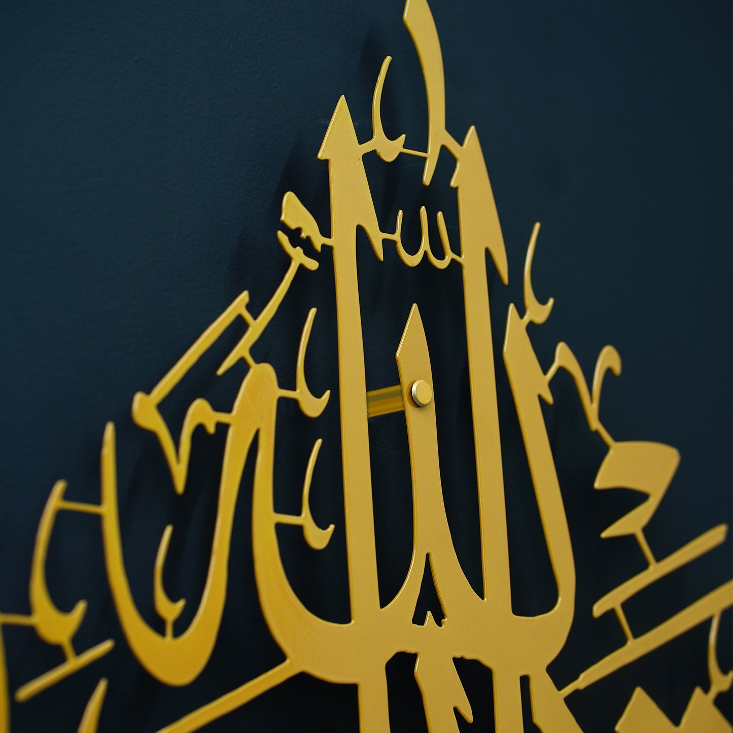 Gold calligraphy La Tahzan İnnallahe Maana, Metal Wall Art featuring Arabic calligraphy of the word 'Allah' mounted on a dark navy blue wall.