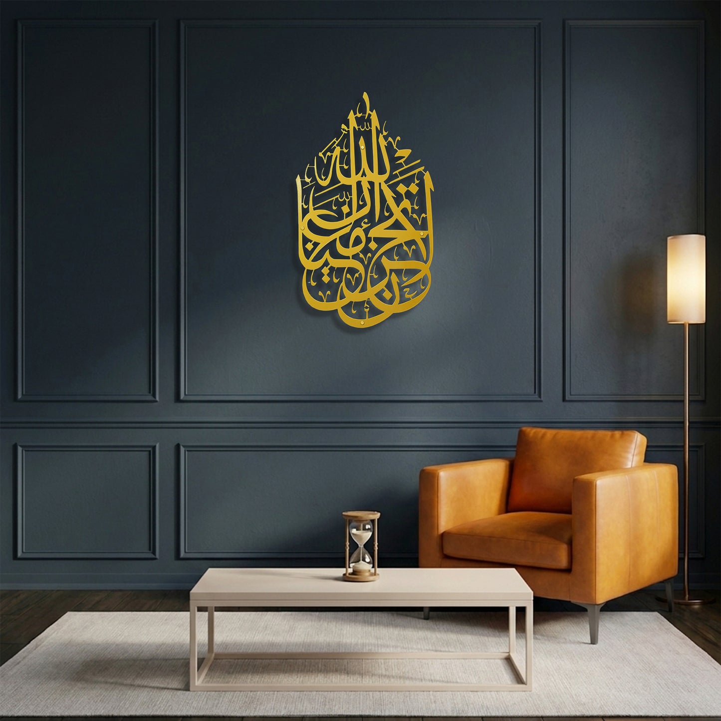 Gold calligraphy La Tahzan İnnallahe Maana, Metal Wall Art mounted on a dark navy blue paneled wall in a modern living room setting with a brown leather armchair, a light wood coffee table and a floor lamp.