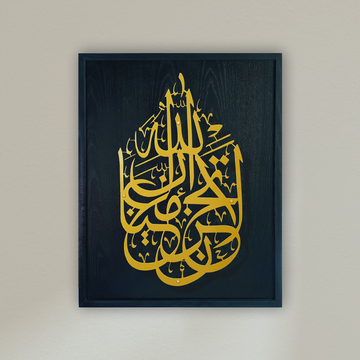 Framed Islamic wall art featuring intricate gold Arabic calligraphy on a blue wooden frame, mounted on a light beige wall.