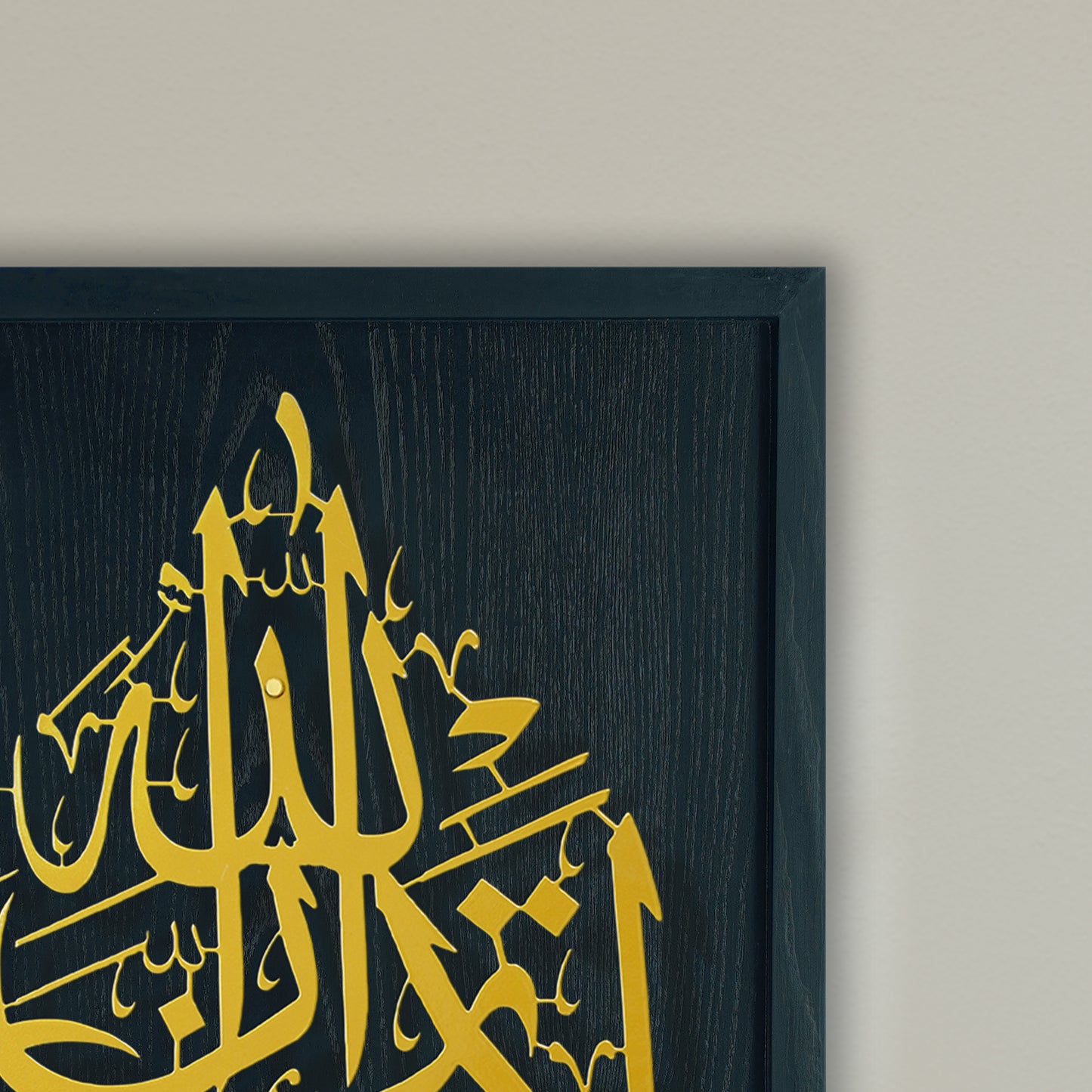 Framed Islamic wall art featuring golden Arabic calligraphy on a black wooden frame, mounted on a light beige wall.