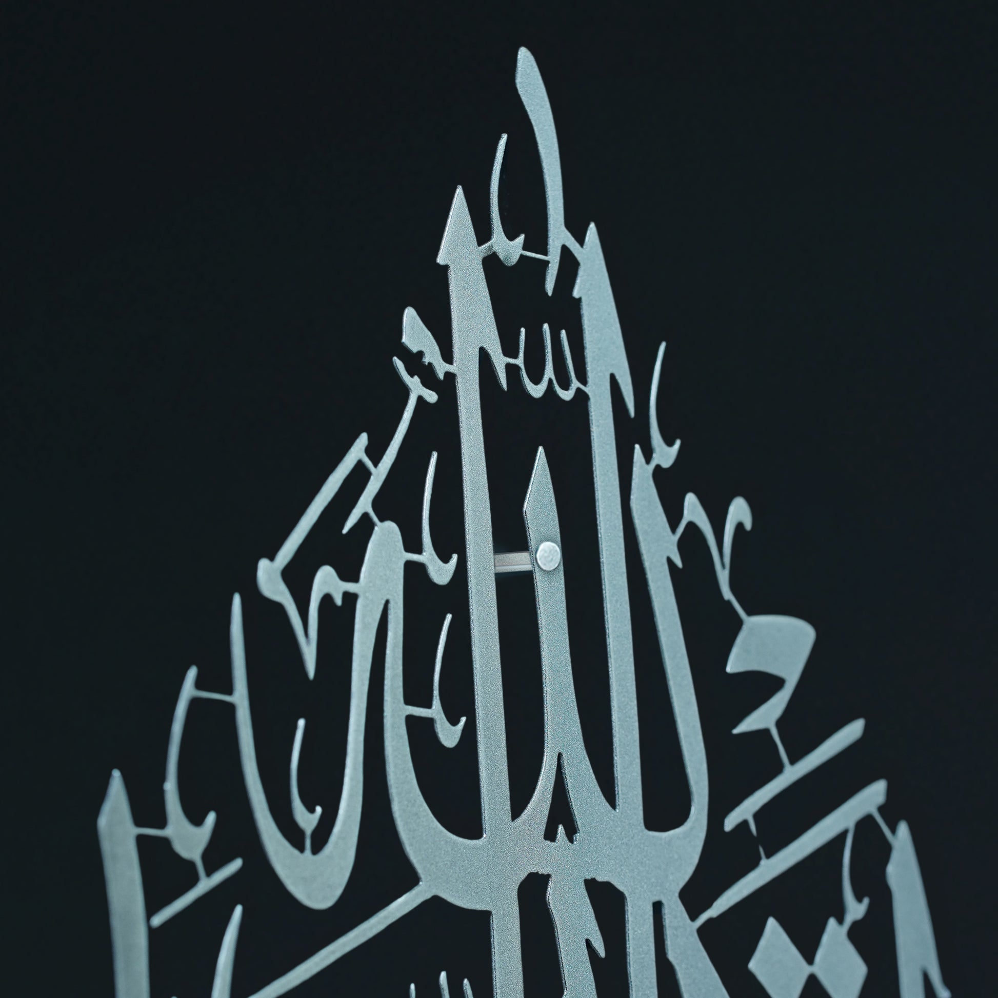 A close-up of a silver metal Islamic wall art piece featuring the word 'Allah' in Arabic calligraphy, mounted against a solid black background.