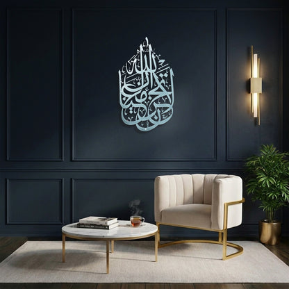 A modern living room setting featuring a large, Silver La Tahzan İnnallahe Maana, Islamic  calligraphy Metal Wall Art piece mounted on a dark navy blue paneled wall. The room is styled with a cream-colored armchair, a round marble-top coffee table with gold legs, a beige rug, and a potted green plant.