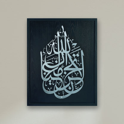 Framed Islamic wall art featuring intricate Arabic calligraphy on a Black wood textured frame, mounted on a neutral beige wall.