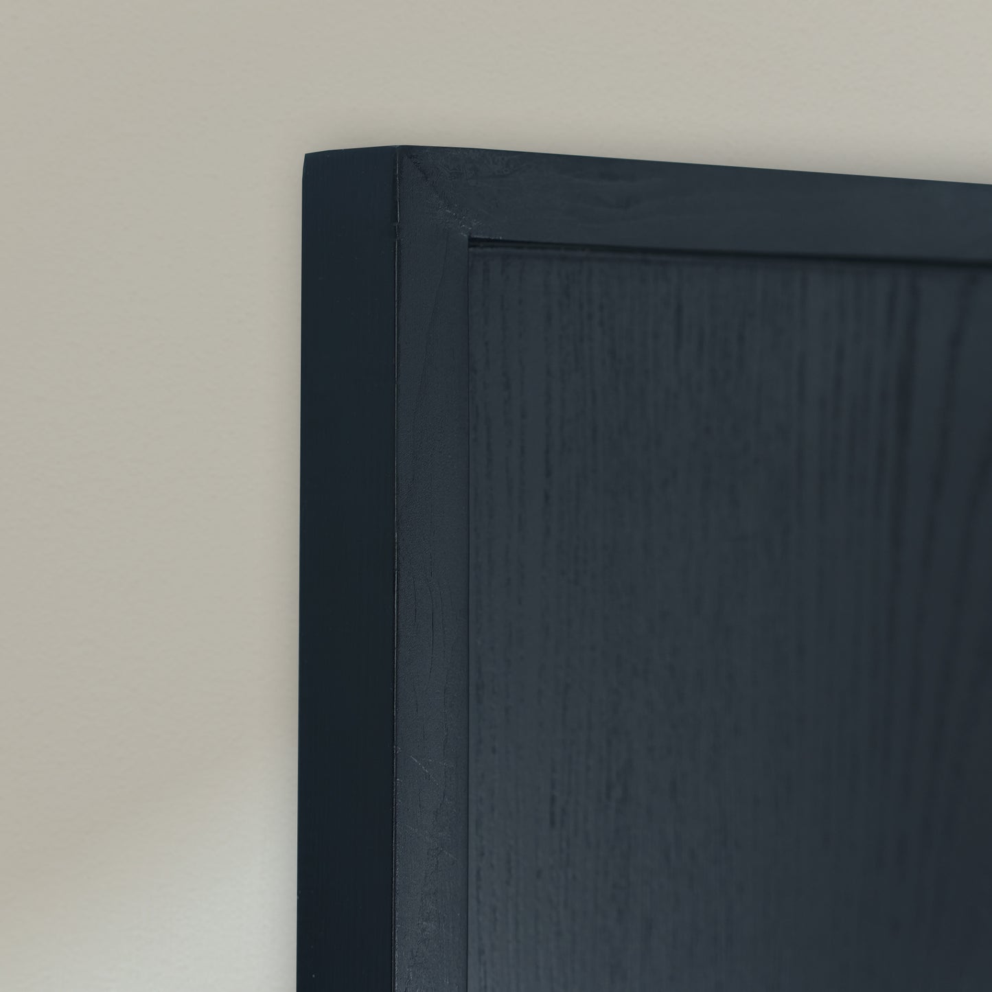Close-up of a Black wooden frame against a plain off-white wall.