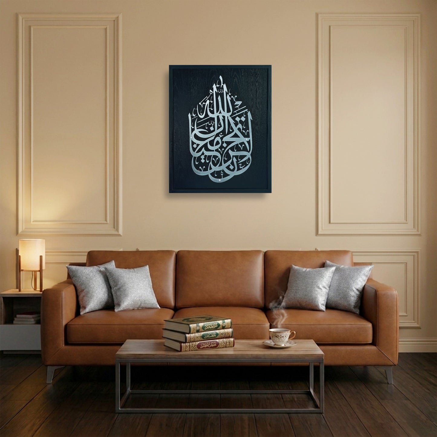 A framed wall art featuring silver Arabic calligraphy on a black wooden frame, displayed above a brown leather sofa in a modern living room setting.