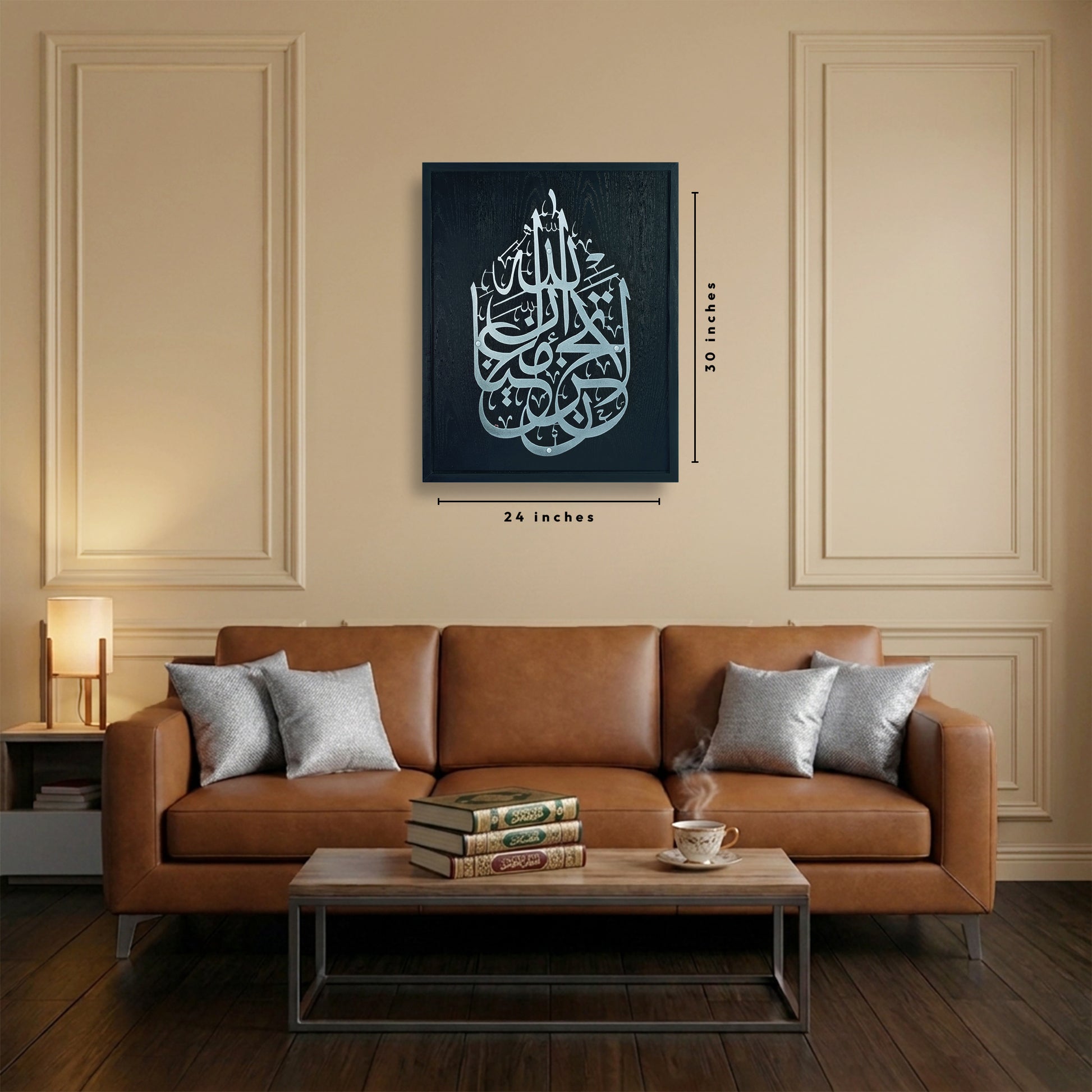 A wood framed wall art silver Arabic calligraphy on a black frame, shown hanging above a brown leather sofa in a styled living room. The image includes dimension labels indicating 24 inches wide by 30 inches tall.